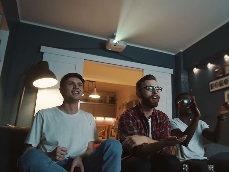 Tre mænd sidder på en sofa i stuen og ser tv