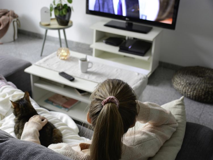 Kvinde sidder i sin sofa, sammen med sin kat, og ser TV