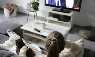 Kvinde sidder i sin sofa, sammen med sin kat, og ser TV