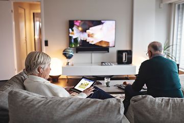 Ældre kvinde sidder i en sofa med hendes tablet, mens hendes mand sidder og ser TV