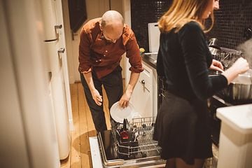 Mand og kvinde i køkkenet. Mand sætter tallerkner i opvaskemaskine, mens kvinden laver mad