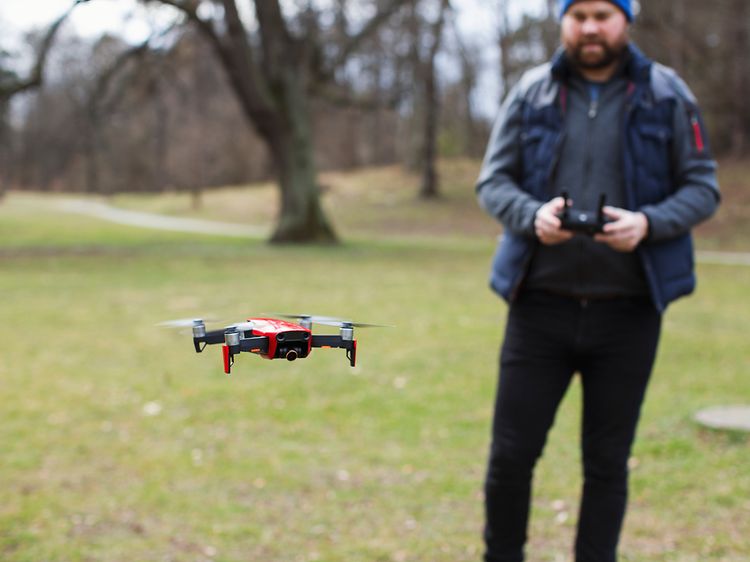 Mand står udenfor, tæt på en skov, og flyver med en drone