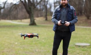 Mand står udenfor, tæt på en skov, og flyver med en drone