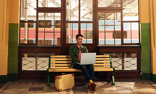 Mand som sidder på en togstation og anvender en Chromebook