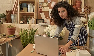 Kvinde i forklæde arbejder på en Chromebook i en blomsterdekoratørs værksted