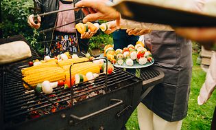 Folk, der står omkring en kulgrill og griller grøntsager