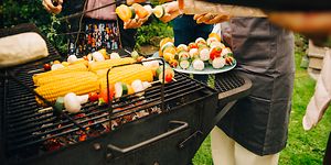 Folk, der står omkring en kulgrill og griller grøntsager
