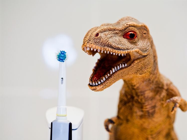 El-tandbørste der står ved siden af en legetøjs dinosaurs