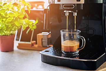 Kaffemaskine der står på et køkkenbord. Kaffemaskinen er igang med at lave en kop kaffe.
