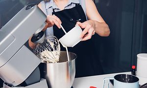 Kvinde der bager en kage i en køkkenmaskine