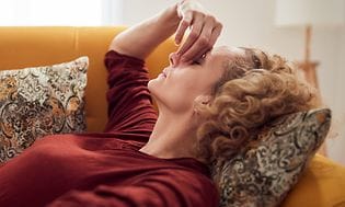 Kvinde med bihulebetændelse og hovedpine, liggende på en sofa