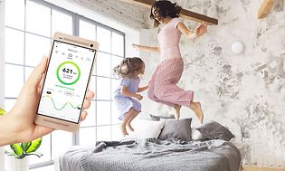 Mor hopper i seng med datter, mens du ser Airthings-appen på en smartphone i forgrunden
