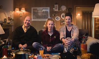 Familie på tre, der sidder på en sofa