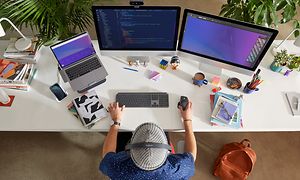 Logitech-WorkBetter-person, der sidder ved et skrivebord med flere skærme og enheder