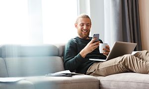 En mand, der bruger sin telefon, mens han har en computer i skødet