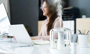 Luftfugter på et skrivebord ved siden af en kvinde, der arbejder på en pc