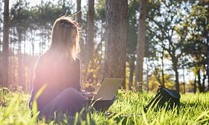Woman sitting in forest with laptop and working
