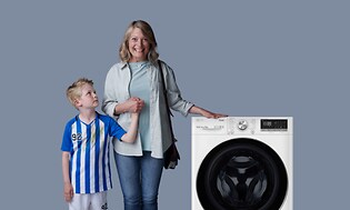 Mor der står foran en vaskemaskine sammen med hendes søn der har beskidt fodboldtøj på