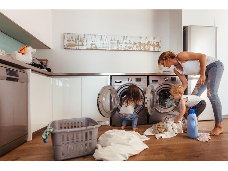 Kvinde og to børn, der lægger tøj i vaskemaskiner på bryggers