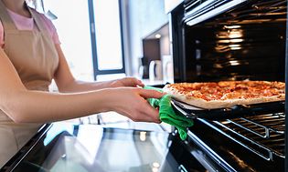 En kvinde, der tager en pizza ud af ovnen