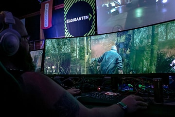 En gamer, der spiller et spil på en bred spilmonitor fra Elgiganten