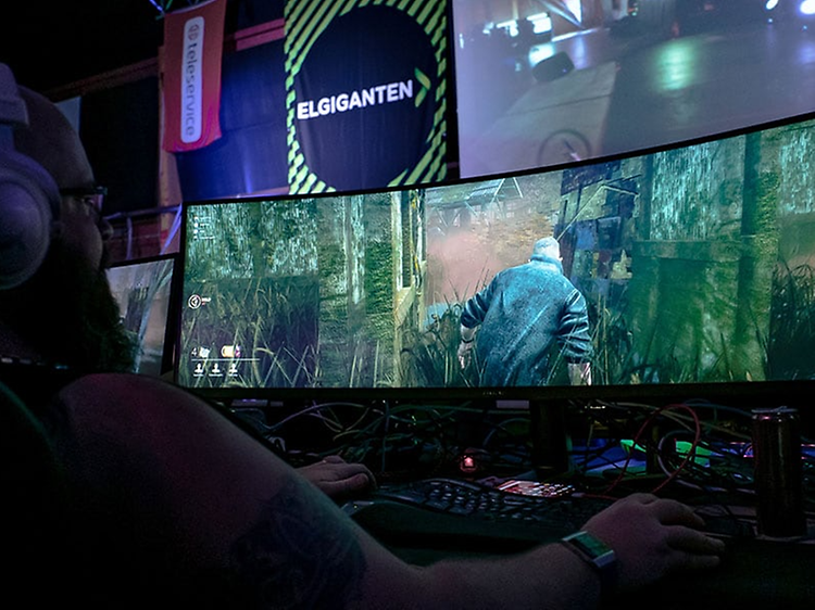 En gamer, der spiller et spil på en bred spilmonitor fra Elgiganten