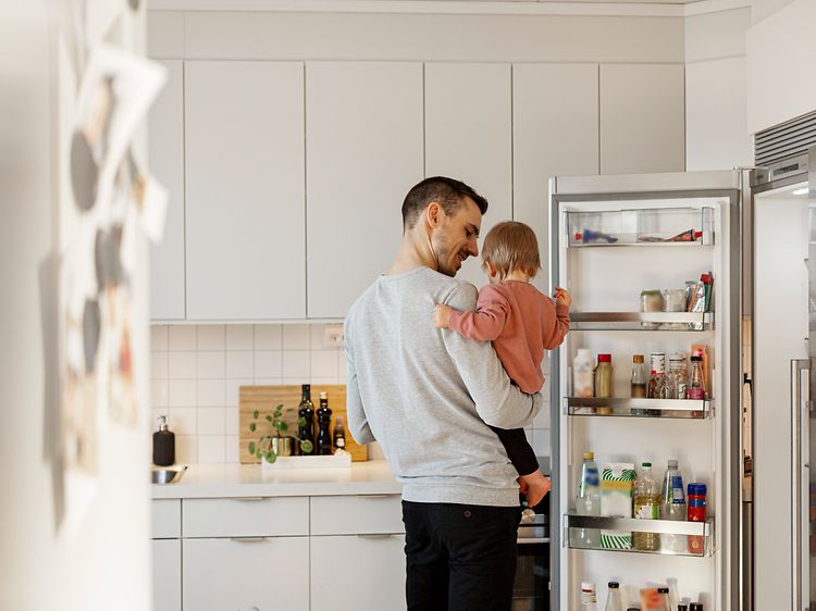 En far og hans datter i deres køkken ved siden af et åbent køleskab