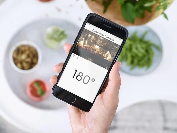 En hånd, der holder en smartphone med en app, der viser kameraet i en smart ovn