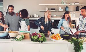Seks mennesker, der laver mad sammen i et stort køkken