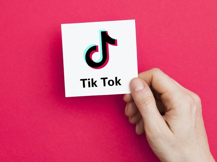 Hånd holder hvidt kort med TikTok-logo på pink baggrund