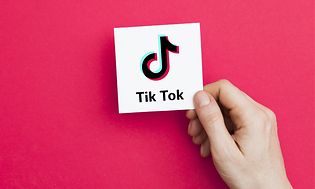 Hånd holder hvidt kort med TikTok-logo på pink baggrund