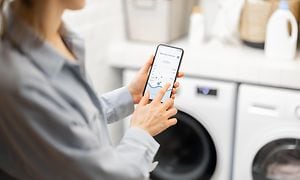 Kvinde kontrollerer vaskemaskine med sin smartphone