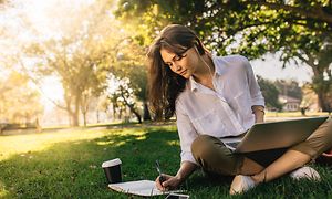 Kvinde sidder i en park, mens hun arbejder på sin laptop