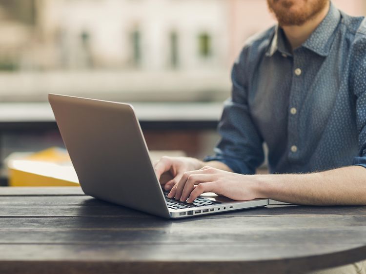 Mand sidder ved et bord og skriver på computer