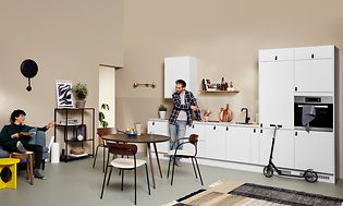 To mænd og et hvidt EPOQ Core-køkken i en åben køkkenløsning, med sofa og spisebord