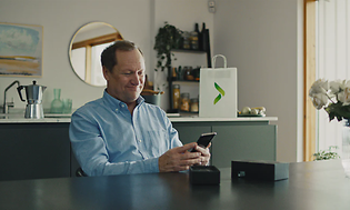 En mand sidder i hans stue og kigger på hans nye mobiltelefon