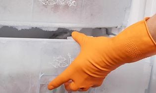 En hånd med handsker på, der åbner en frossen fryseskuffe