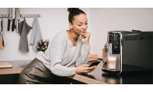 En kvinde med en smartphone foran sin Melitta kaffemaskine