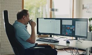 Mand sidder foran hans stationære computer og arbejder, mens han nyder en kop kaffe.