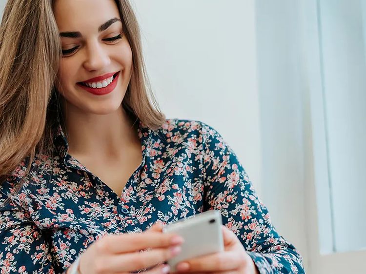 Smilende kvinde, der sidder med sin telefon I hånden