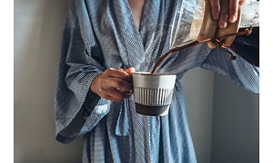 En kvinde i en morgenkåbe, der hælder en friskbrygget kop kaffe op