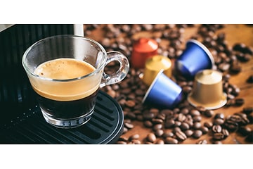 En kop espresso fra en kapselmaskine med kapsler og kaffebønner på disken