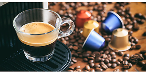 En kop espresso fra en kapselmaskine med kapsler og kaffebønner på disken
