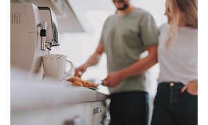 En kaffemaskine og et par, der står i baggrunden