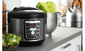 En sort slow cooker på et køkkenbord med grøn salat foran