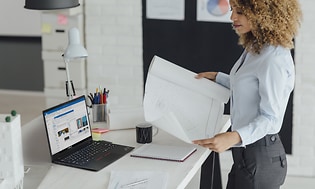 Kvindelig arkitekt ser på et bueprint med Lenovo ThinkPad ved siden af hende på et bord