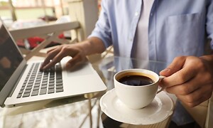 Person drikker kaffe lige ved siden af en bærbar computer