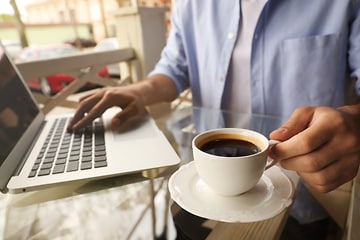 Person drikker kaffe lige ved siden af en bærbar computer