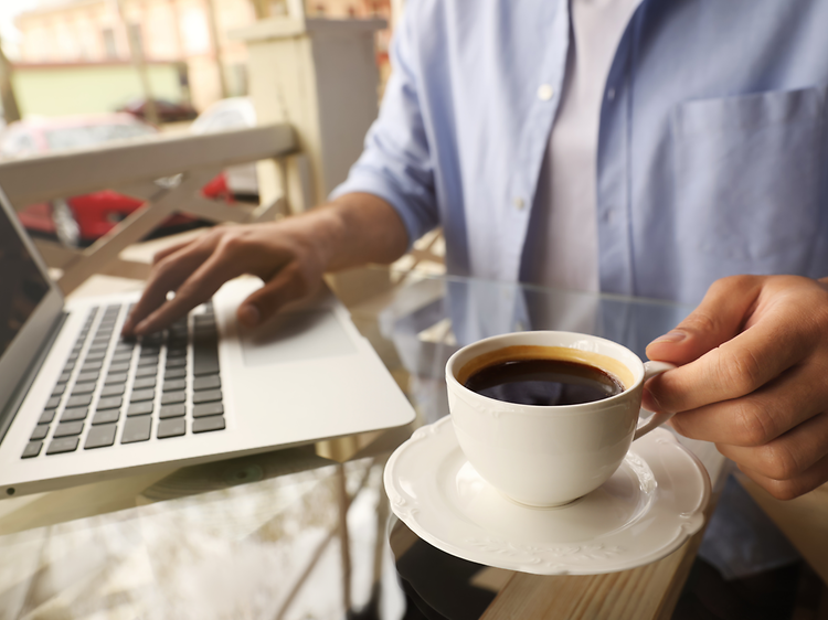 Person drikker kaffe lige ved siden af en bærbar computer