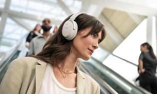 Bose hovedtelefoner-Kvinde med Bose QC45 hovedtelefoner på en rulletrappe